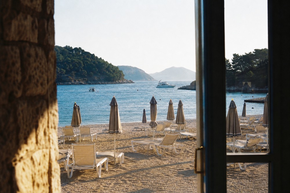 Sun loungers and umbrellas in rows on sand beside calm blue water