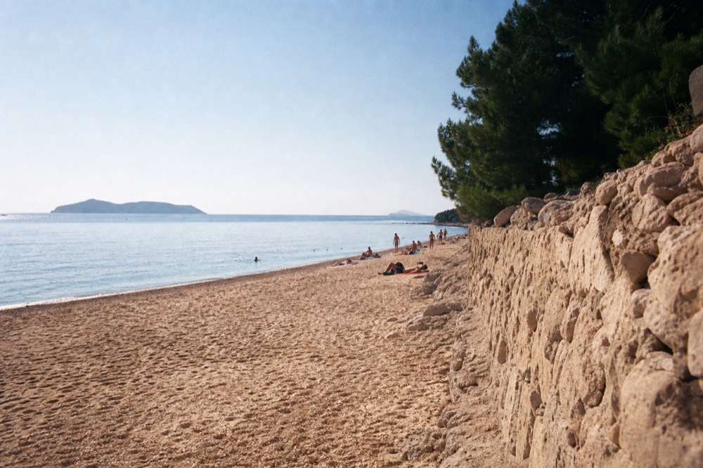 A sandy beach in late afternoon light with calm water and a distant island silhouette
