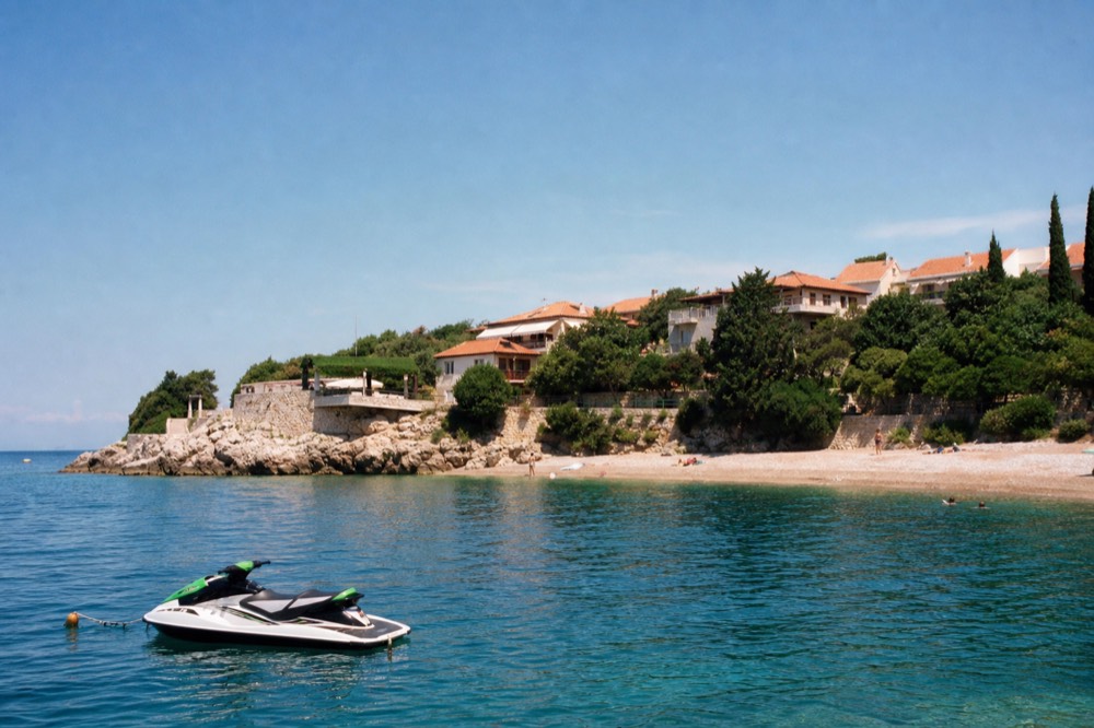 A jet ski sitting on calm water beside a sandy beach with a rocky headland behind