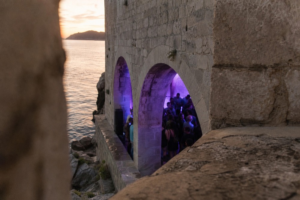 A crowd dancing under stone vaults lit by purple and blue lights