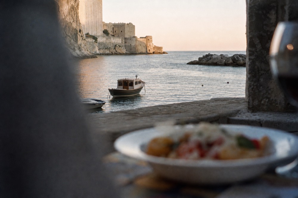 A small boat at anchor in a quiet harbour at dusk with a plate of food on a table