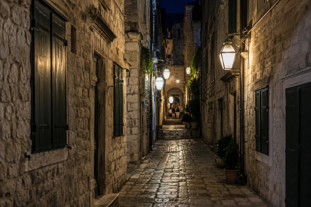 A narrow stone lane lit by lanterns at night with closed shutters