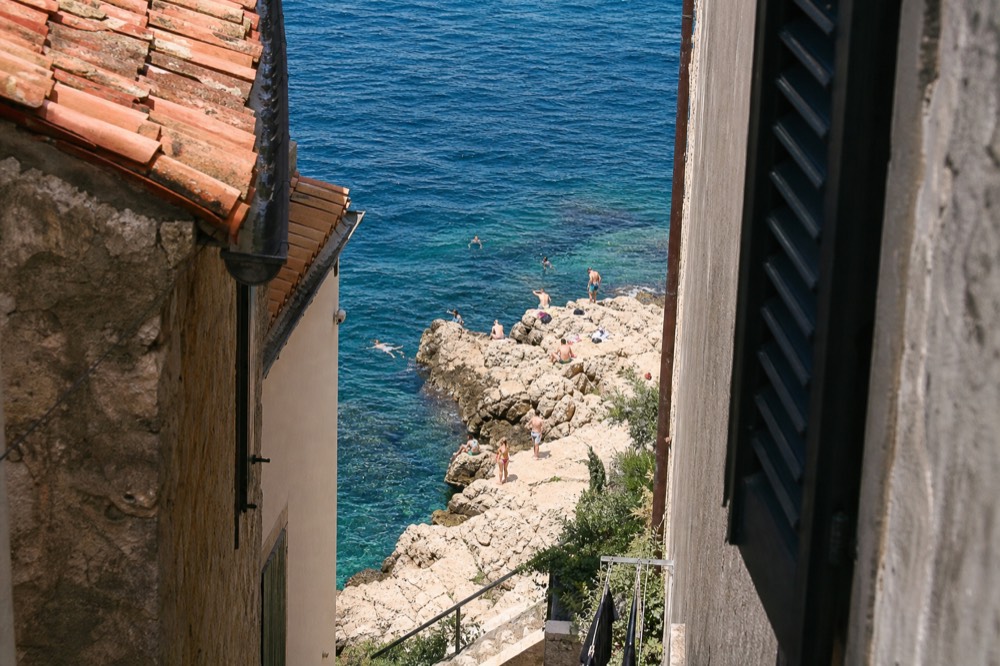 Swimmers on rocky shoreline beside clear water near Dubrovnik