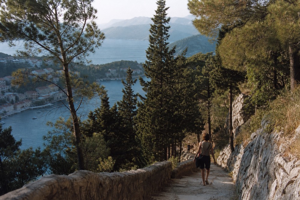 A mountain road overlooking a blue bay with a small town at the water's edge