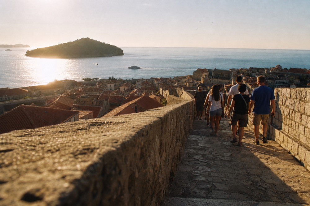 Visitors walking the Dubrovnik city walls above red rooftops with the Adriatic Sea beyond
