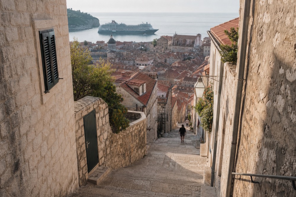 A large cruise ship anchored offshore beyond the Dubrovnik Old Town rooftops