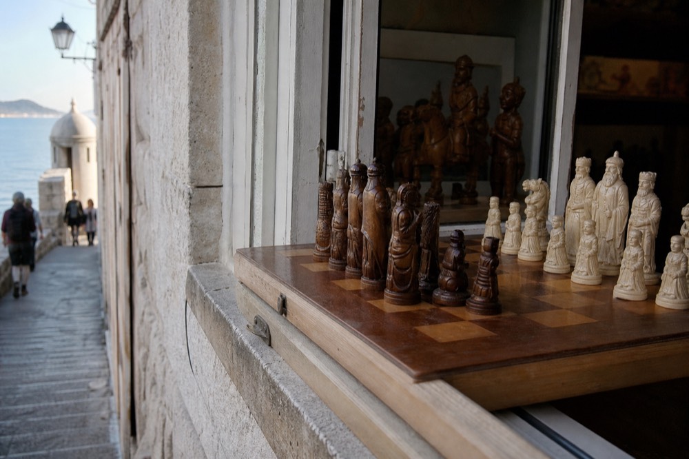 A close view of carved wooden chess pieces arranged on a board beside an open workshop window