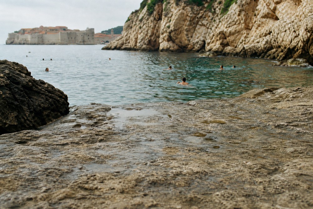 Swimmers in clear turquoise water beside rocky cliffs near Dubrovnik