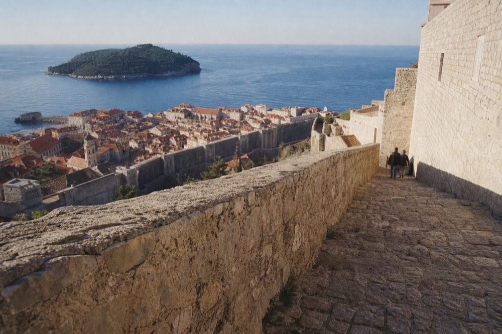 The city walls walkway above red rooftops with the island of Lokrum in the distance