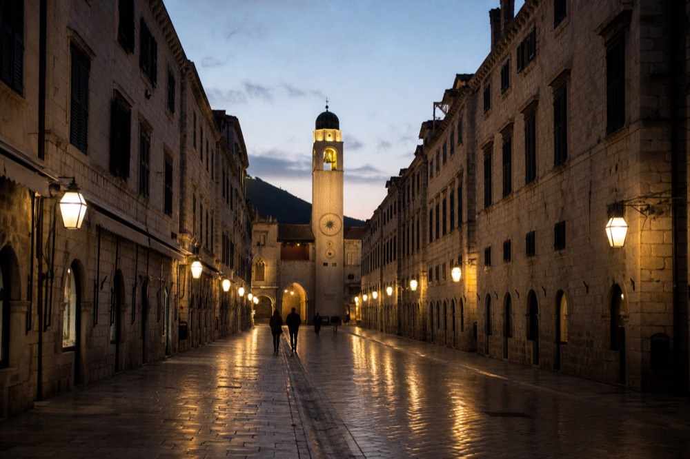 The illuminated bell tower and Stradun at dusk in winter with empty street and warm window light