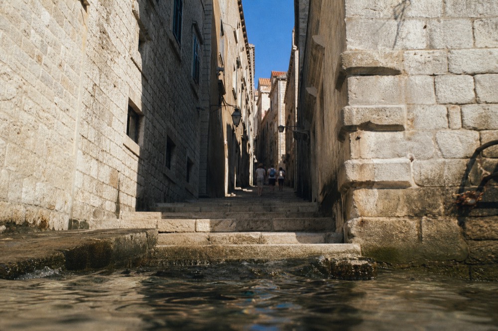 A narrow stepped lane in Dubrovnik Old Town between tall stone buildings