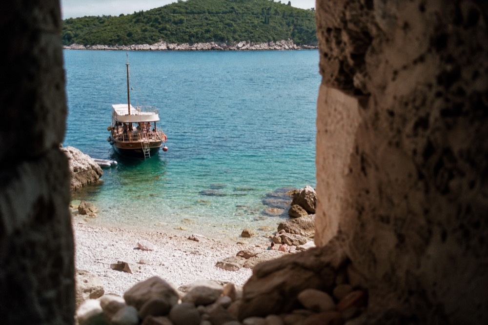 A wooden boat anchored in a turquoise cove beside a green island