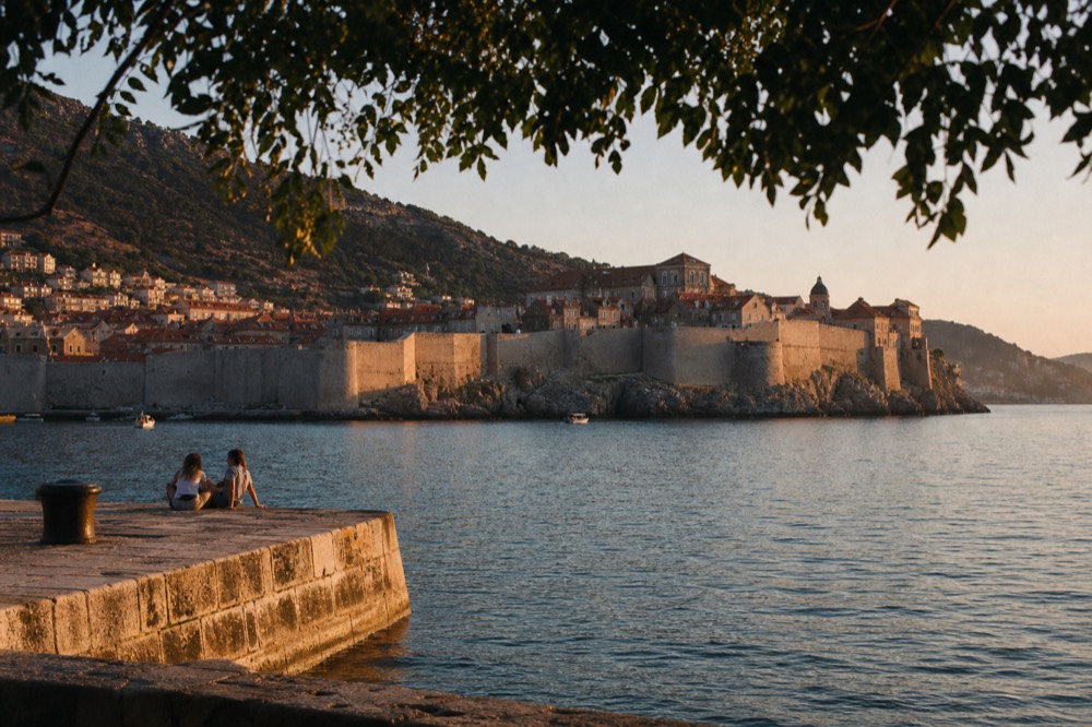 A walled old town seen from the sea at dusk with warm light on stone ramparts