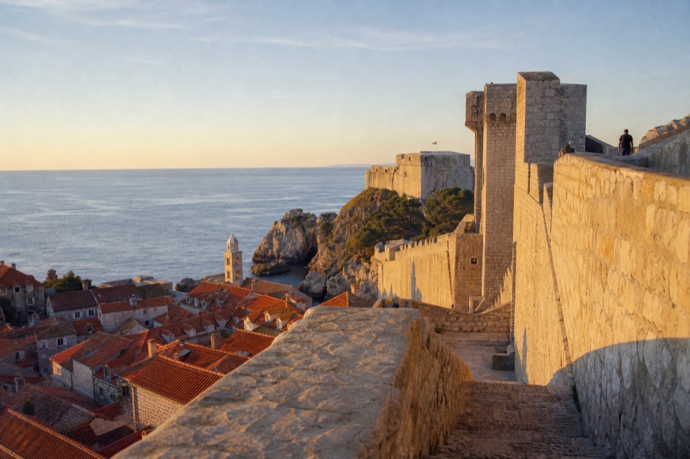 Stone city walls rising above red rooftops and a calm sea
