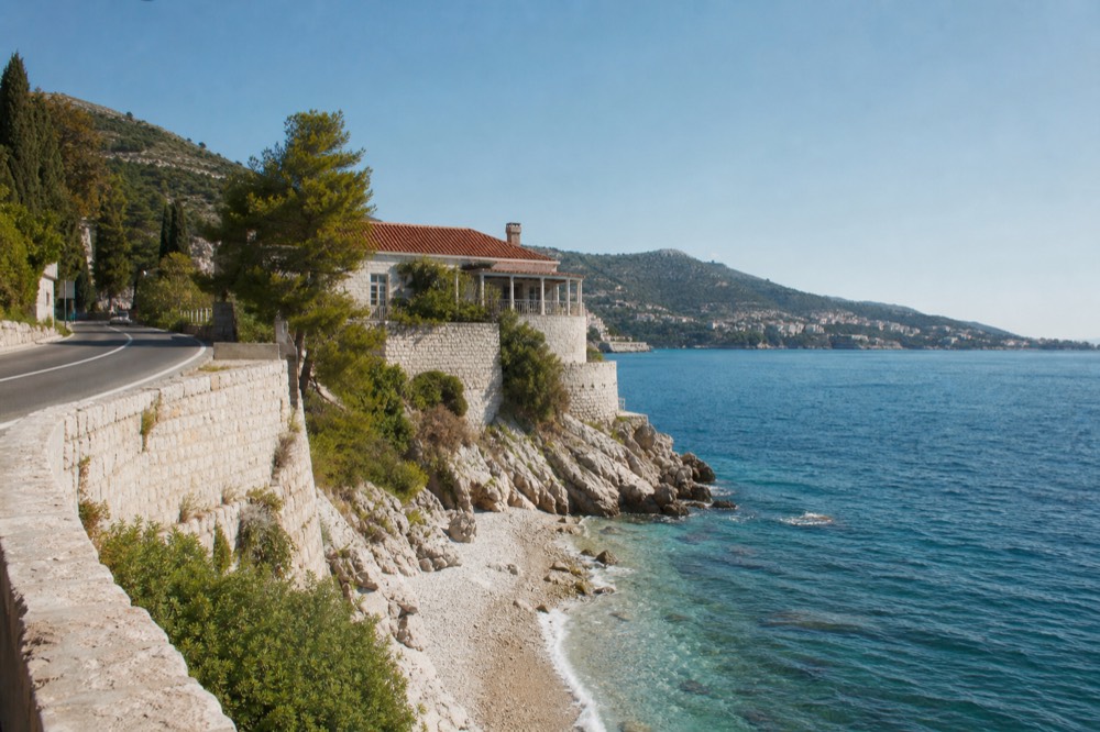 A coastal road curving along a rocky shoreline with hills