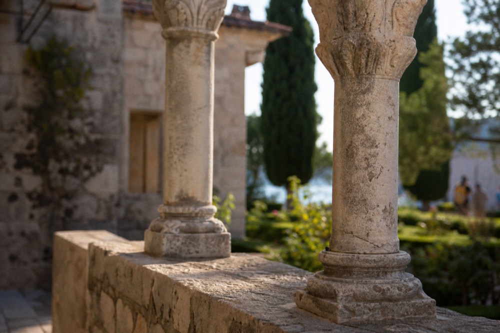 Stone monastery cloister surrounded by gardens and tall cypress trees