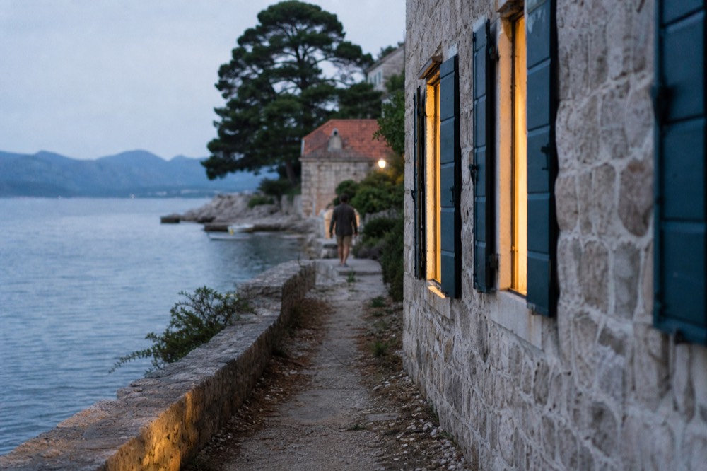 Island coastline in warm late-afternoon light with calm sea and distant hills