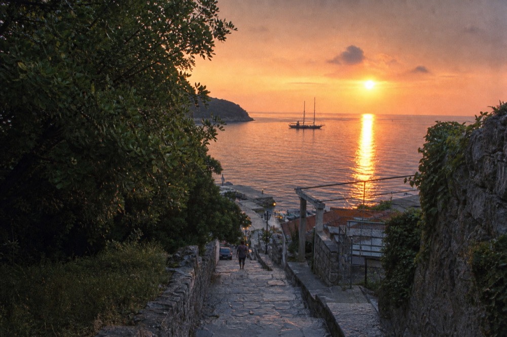 A sailing ship silhouetted against an orange sunset over the Adriatic sea