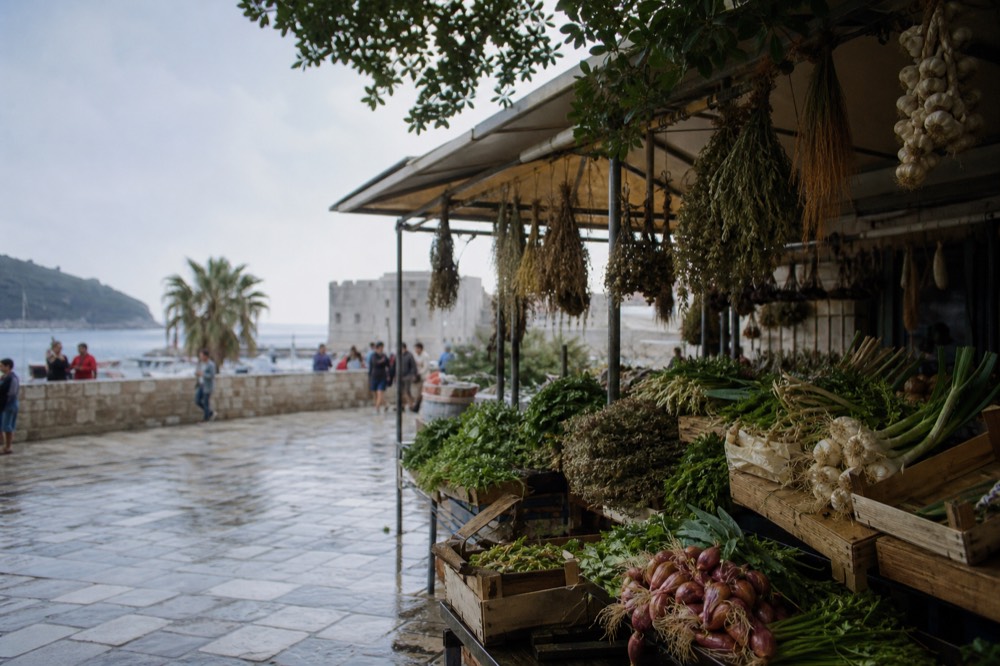 A busy market stall with fresh vegetables and dried herbs under an awning