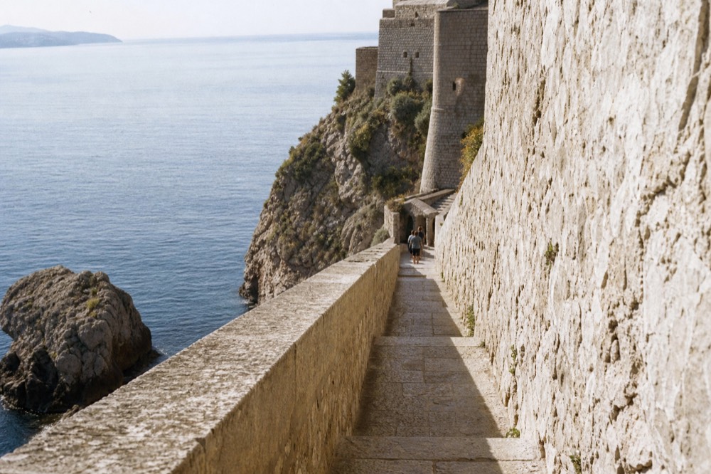 Walking path along the sea outside high stone city walls in early morning light