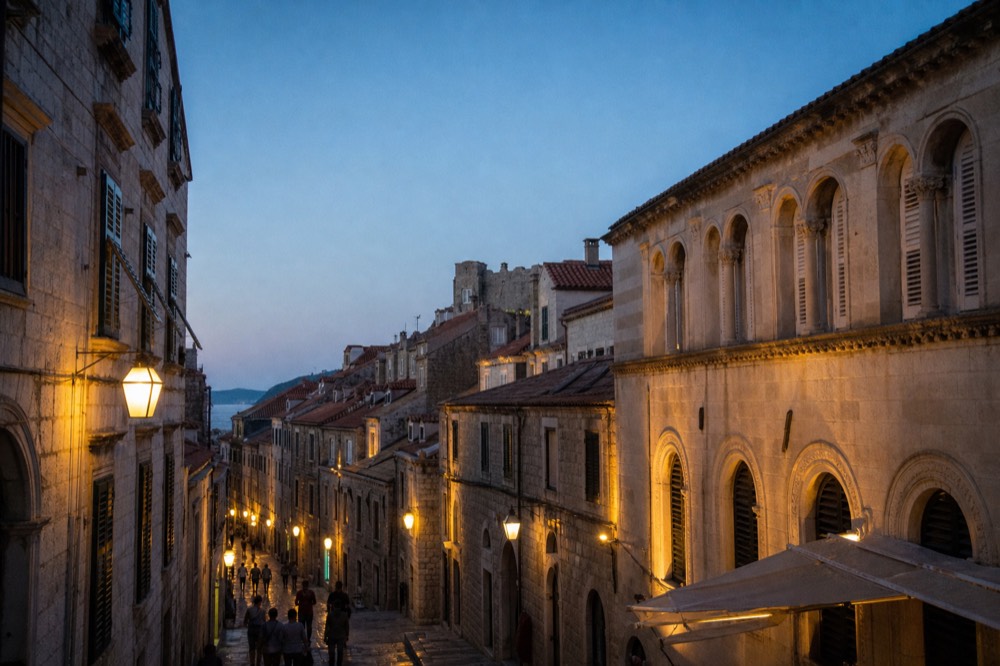 Evening view of a narrow lamplit stone street in Dubrovnik with warm light on baroque facades