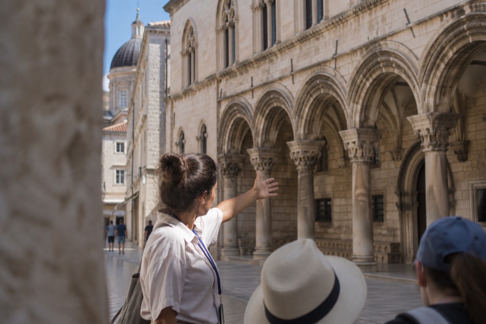 A local guide gesturing toward the Sponza Palace facade on a quiet morning street