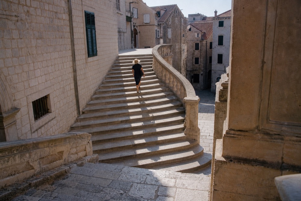 A wide baroque staircase in Dubrovnik curving up between stone balustrades