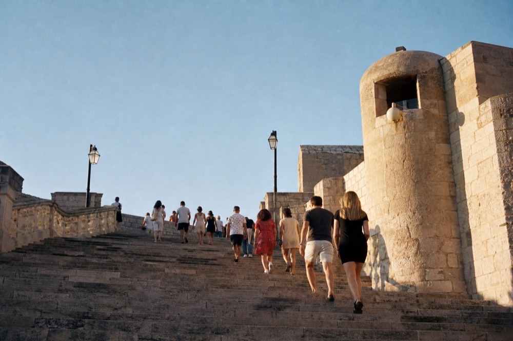 Visitors climbing a wide stone staircase in Dubrovnik, worn treads in bright daylight