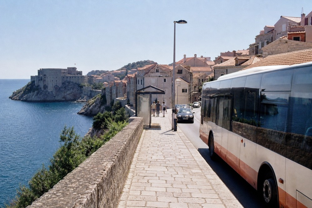 A local city bus at a stop on a sunny street near the coast