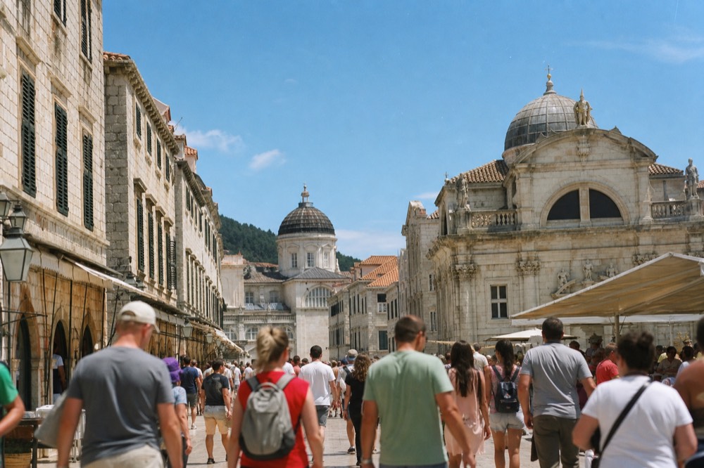 Crowded stone square in Dubrovnik with streams of visitors walking between historic buildings