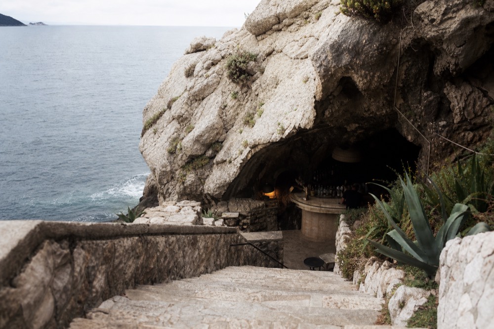 A stone staircase descending into a dim natural cave with a bar counter inside