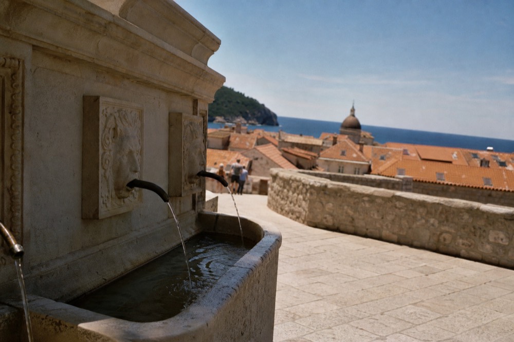 Stone fountain with carved maskeron spouts at the edge of a paved square