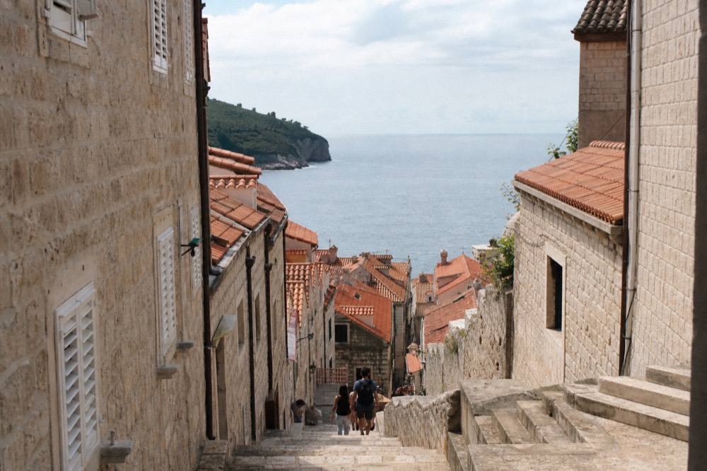 Sunlit limestone street in Dubrovnik Old Town with stone staircases rising on both sides