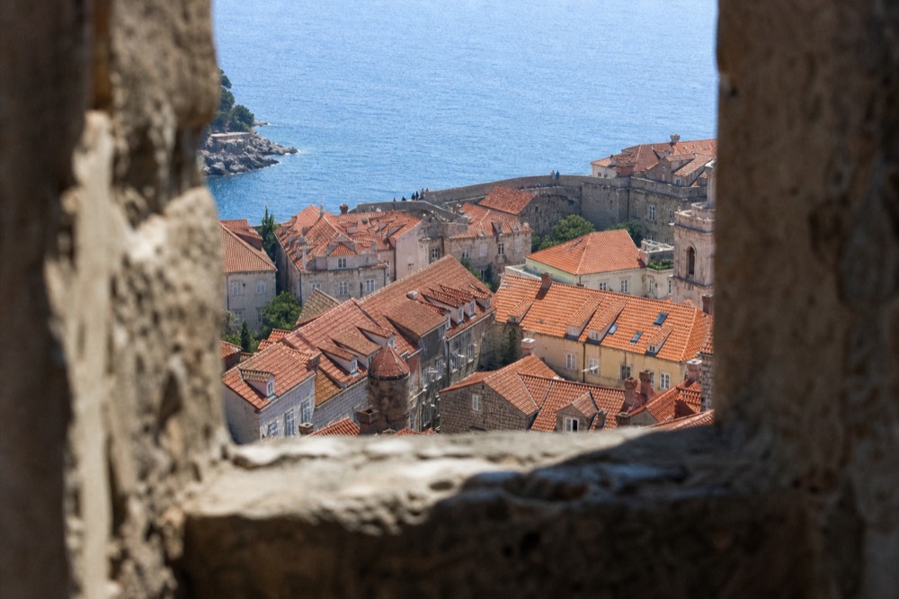 Terracotta rooftops of a walled old town seen from a high stone tower above the sea