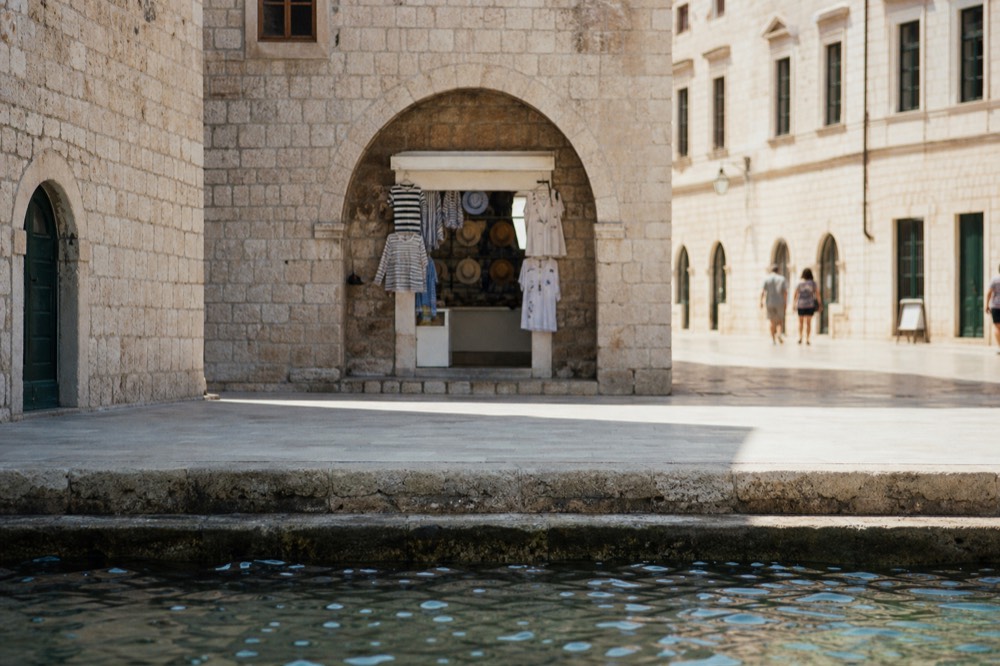 A small shopfront under a stone arch on a sunlit Dubrovnik street