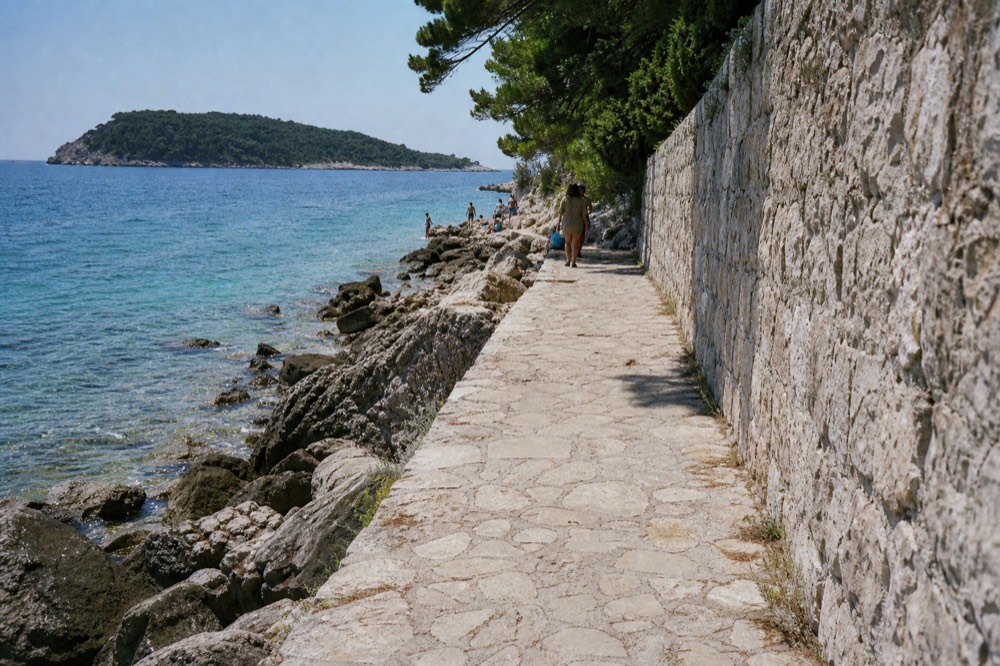 Clear turquoise water over a pebble beach near Dubrovnik with the island of Lokrum behind