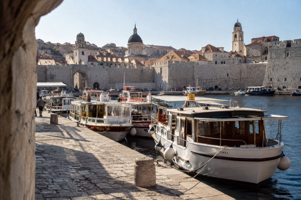 A stone quay with ticket boats and the walled city rising behind