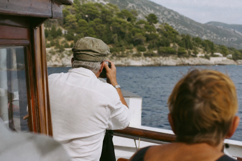 A boat deck with passengers looking out at island coastline on a sunny day
