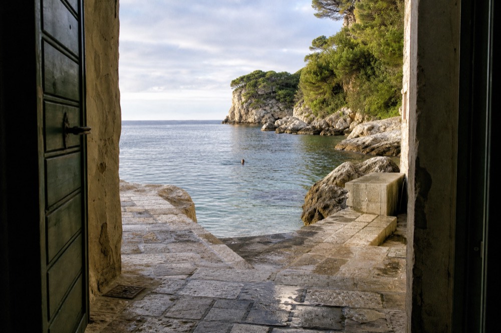 A swimmer in clear water near a rocky Adriatic cove in warm evening light