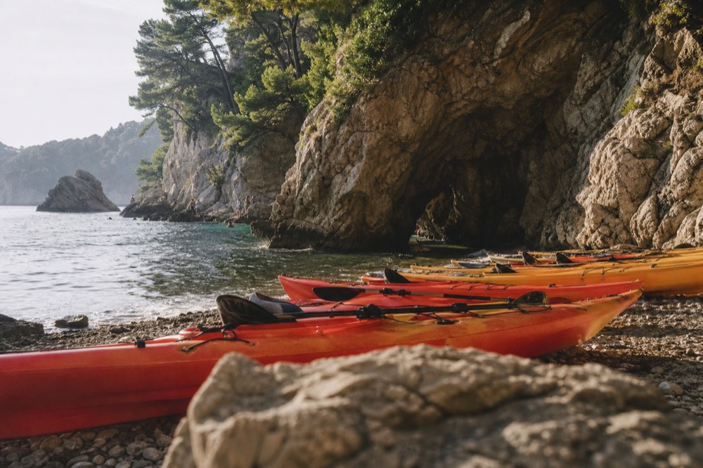 Row of kayaks pulled onto a pebble beach beside a sea cave entrance