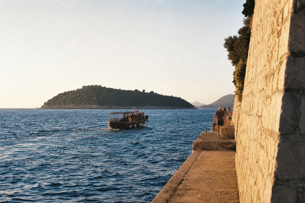 A wooden boat crossing open blue sea toward a green island
