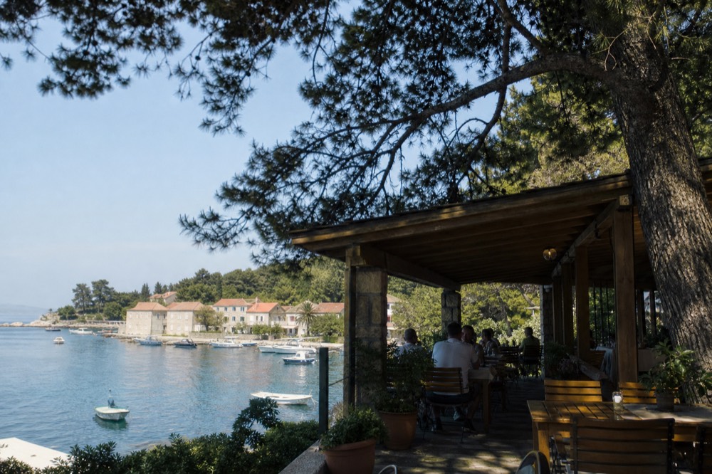 A shaded restaurant terrace above a small island harbour at midday
