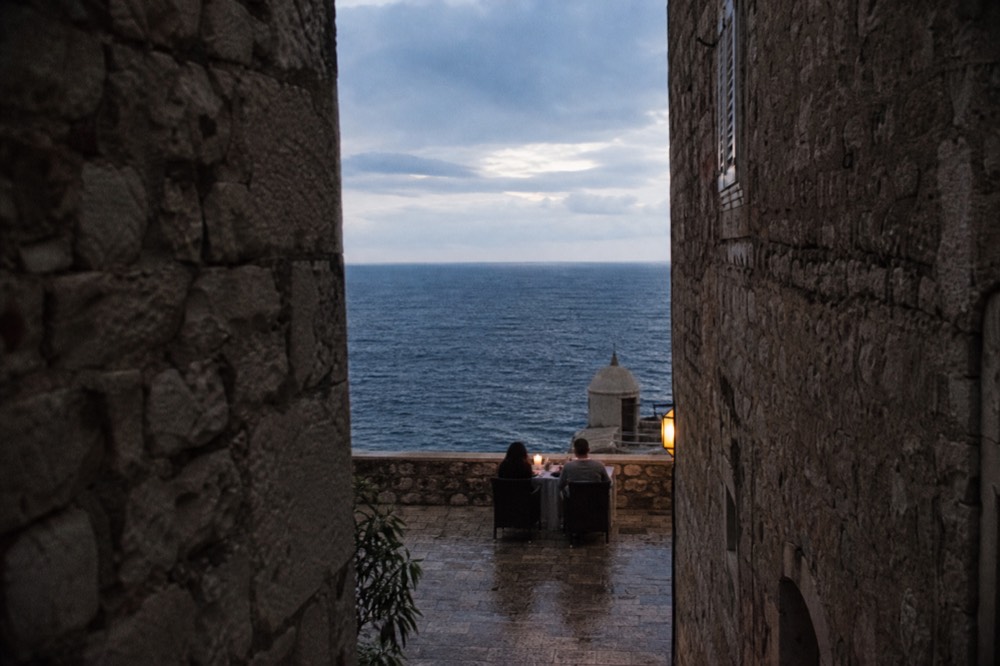 Candlelit table for two on a stone terrace overlooking a dark Adriatic sea