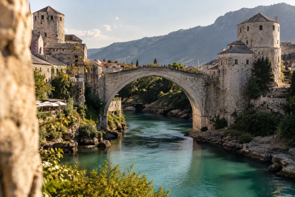 Stone bridge arching over a turquoise river with old towers on both banks