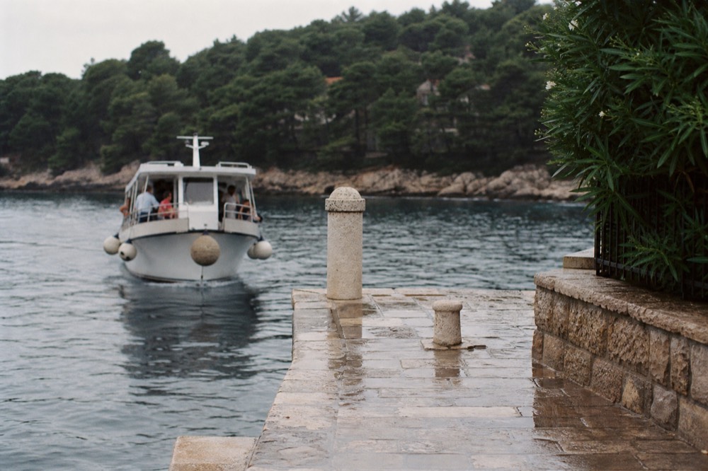 A small ferry approaching a stone quay on a green island coastline
