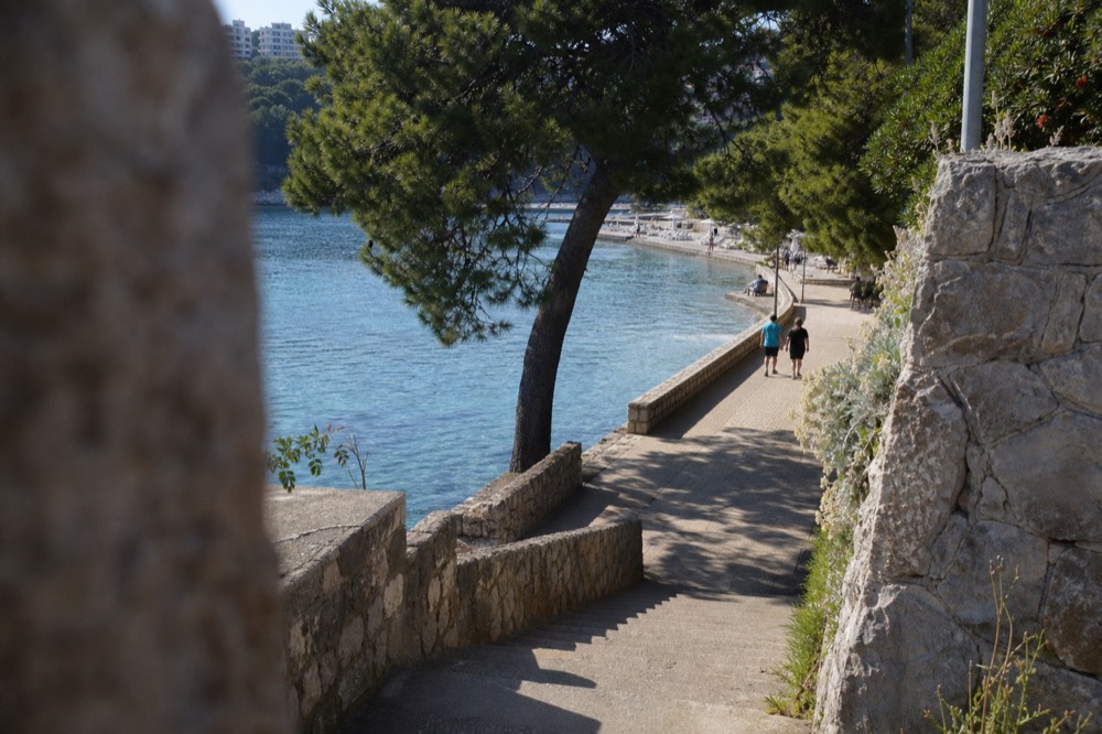 Lapad Beach with calm clear water and a promenade lined with trees
