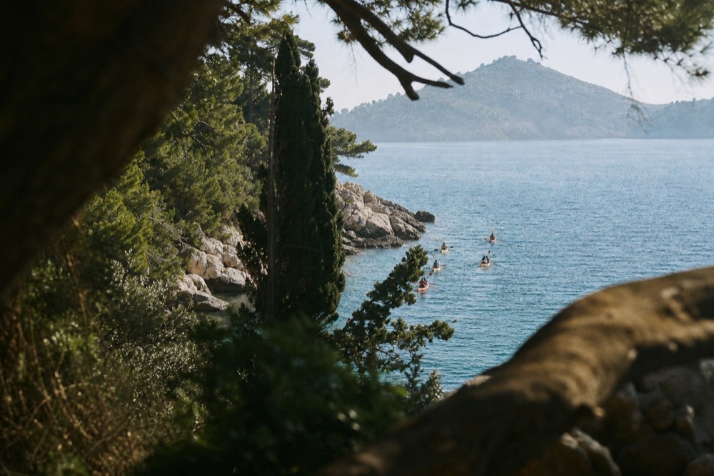 Sea kayakers paddling along pine covered cliffs toward Lokrum island
