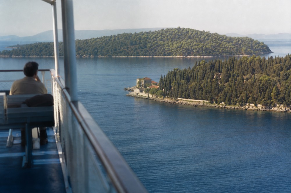 A wooded island seen across clear water from a boat deck