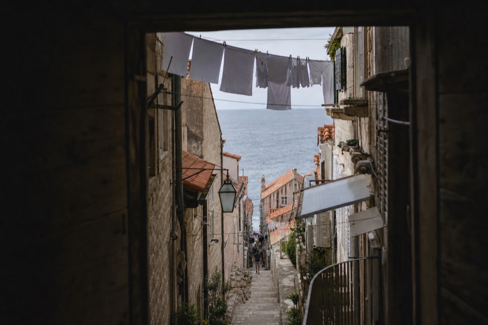 Steep stone staircase between old buildings with laundry above and shaded walls