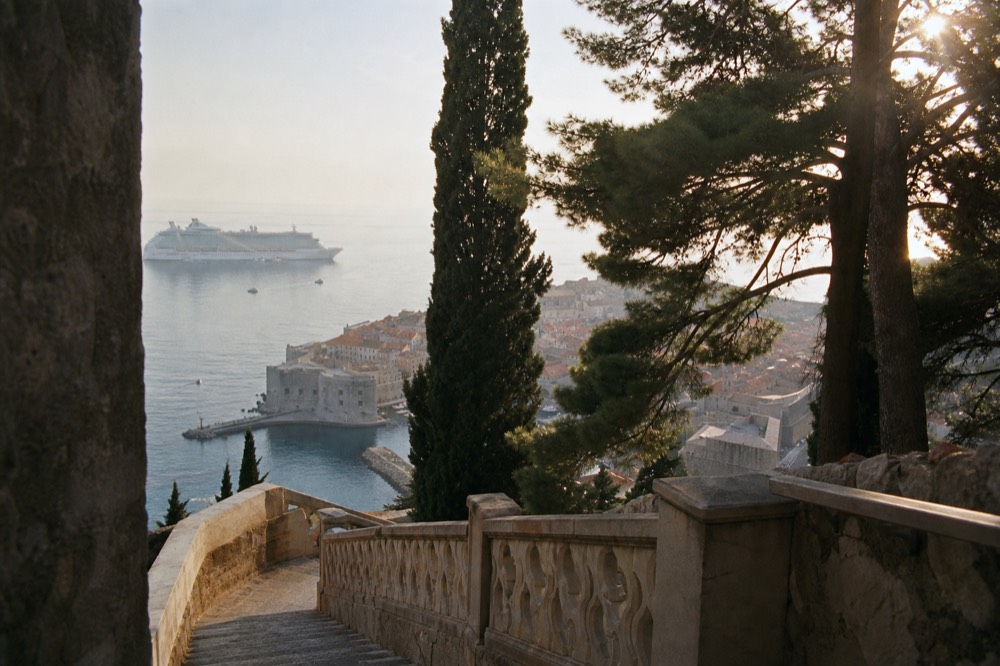 A large cruise ship anchored on open water outside a walled coastal town